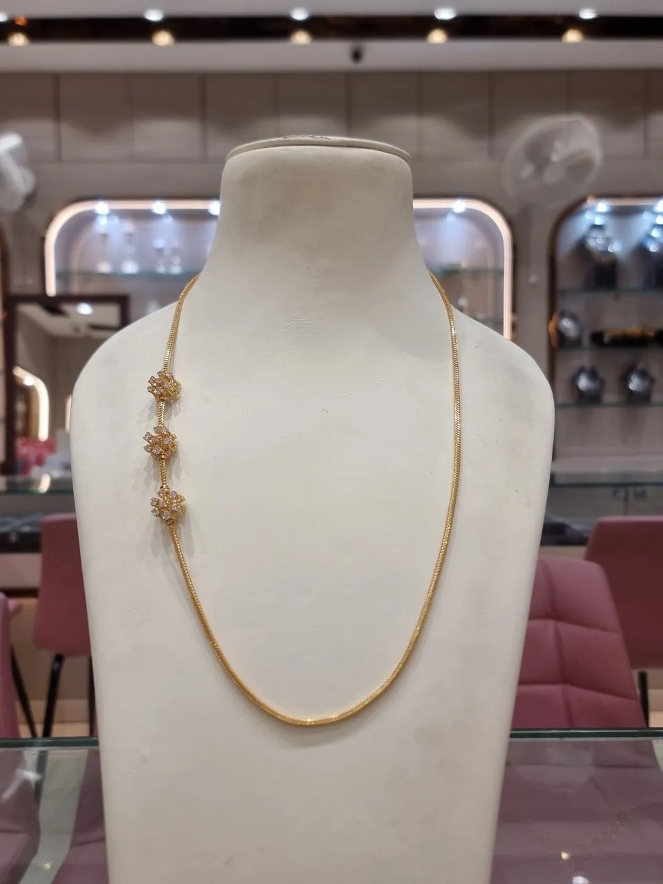 The phone photo: a gold chain with three flower motifs on a white display bust in a jewellery shop
